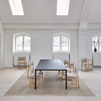 Minimalist black dining table surrounded by light beige and cream chairs on a soft beige rug in a bright, airy room.