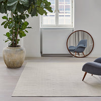 Neutral beige area rug in a modern interior with a blue accent chair and green plant, reflecting a minimalist style.