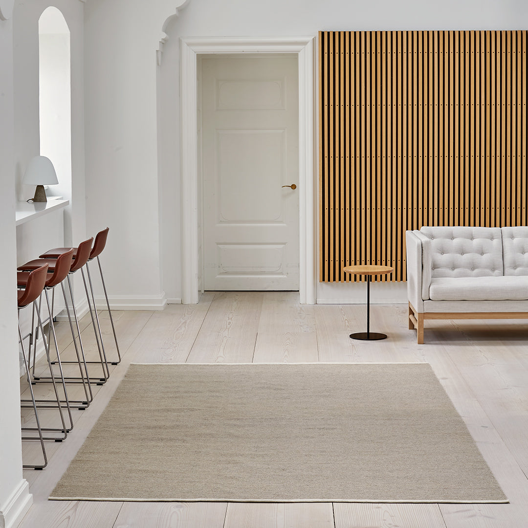 Beige area rug on light wooden floor, complemented by a textured wooden wall and minimalist decor.