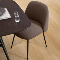 Textured brown upholstered chair with sleek black metal legs, complementing a dark wooden table. Modern design aesthetic.
