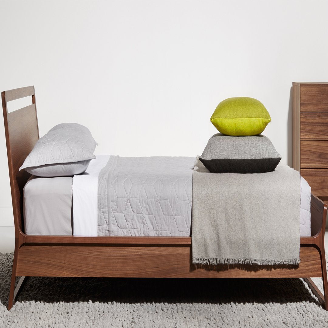 "Modern bed with grey linens, textured beige throw, and vibrant green, grey, and black pillows."