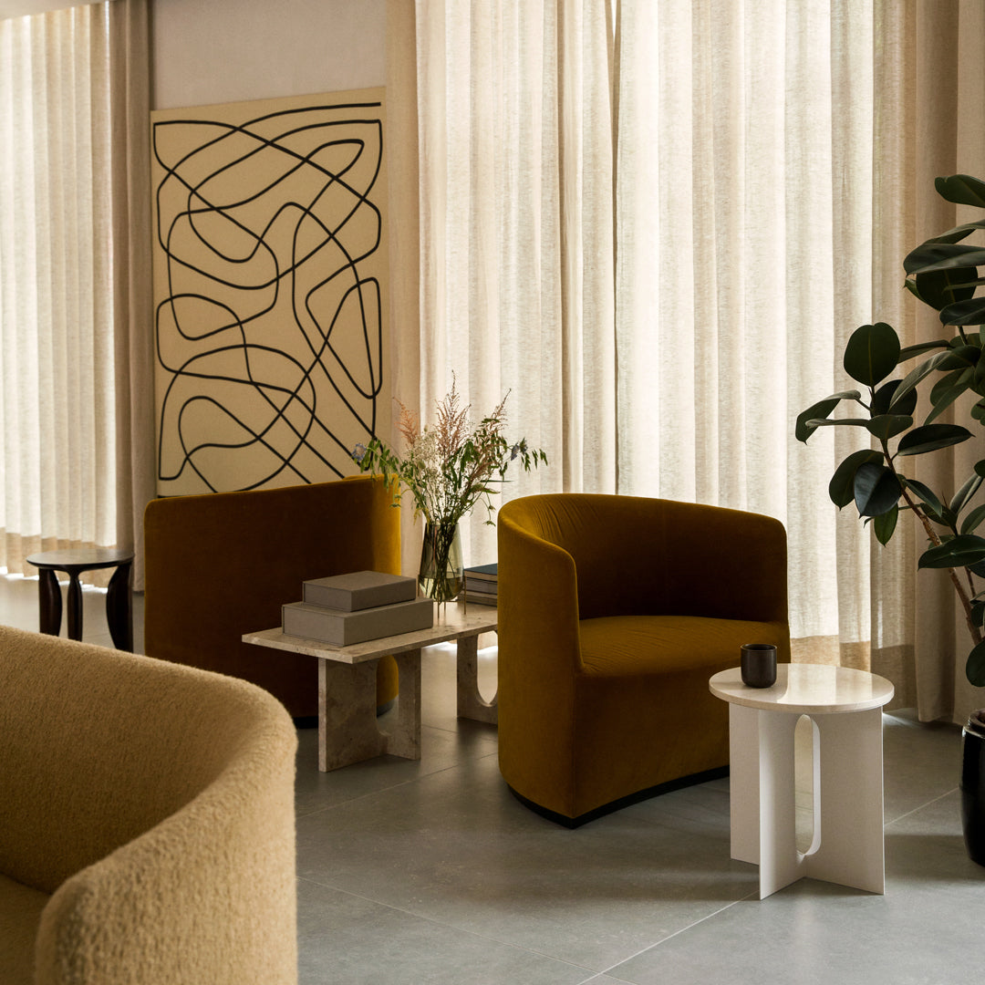 Modern space featuring mustard yellow armchairs, neutral tones, and abstract wall art with black lines against soft curtains.