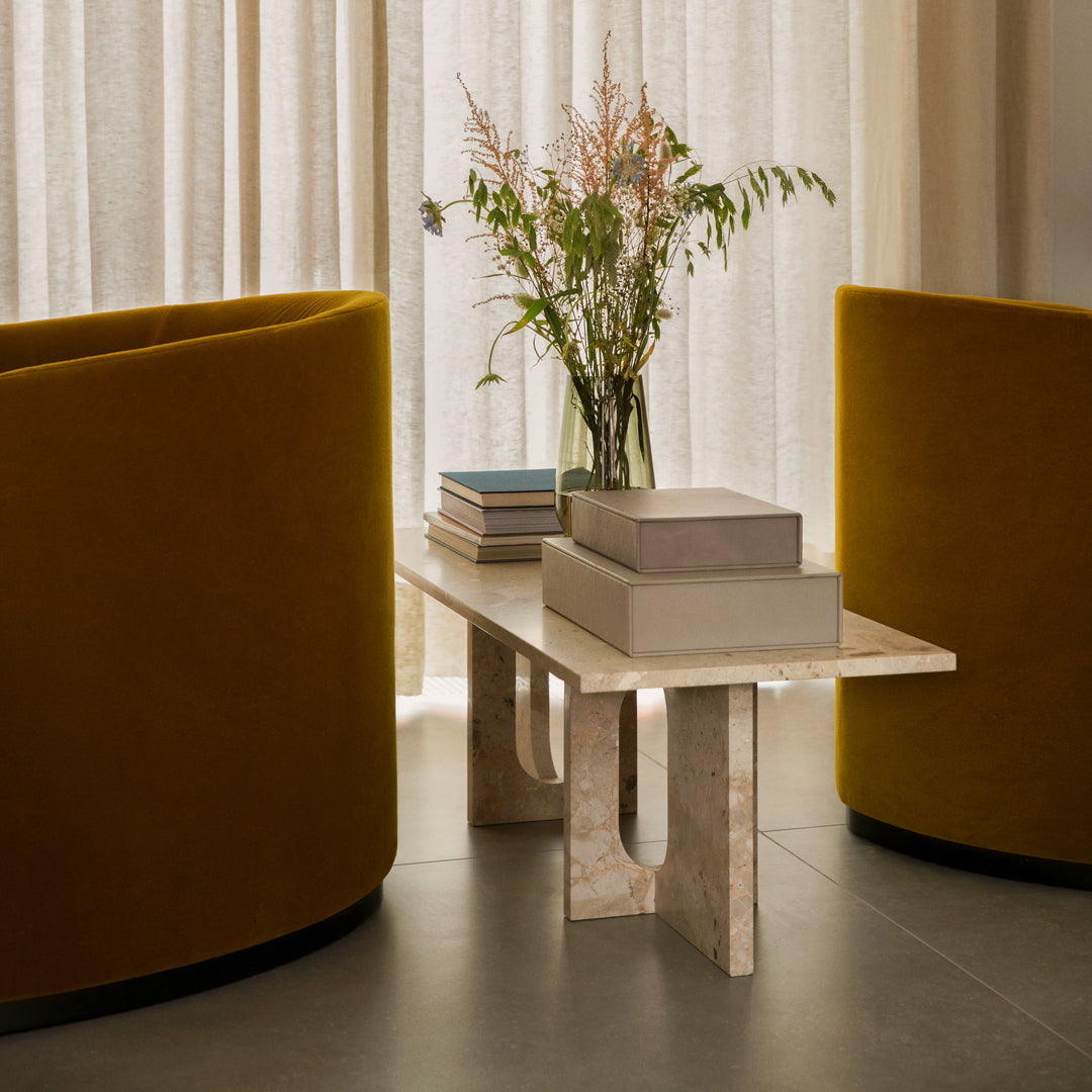 "Yellow velvet chairs and a textured cream coffee table in a modern living space, accented with soft floral decor."