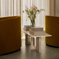"Yellow velvet chairs and a textured cream coffee table in a modern living space, accented with soft floral decor."