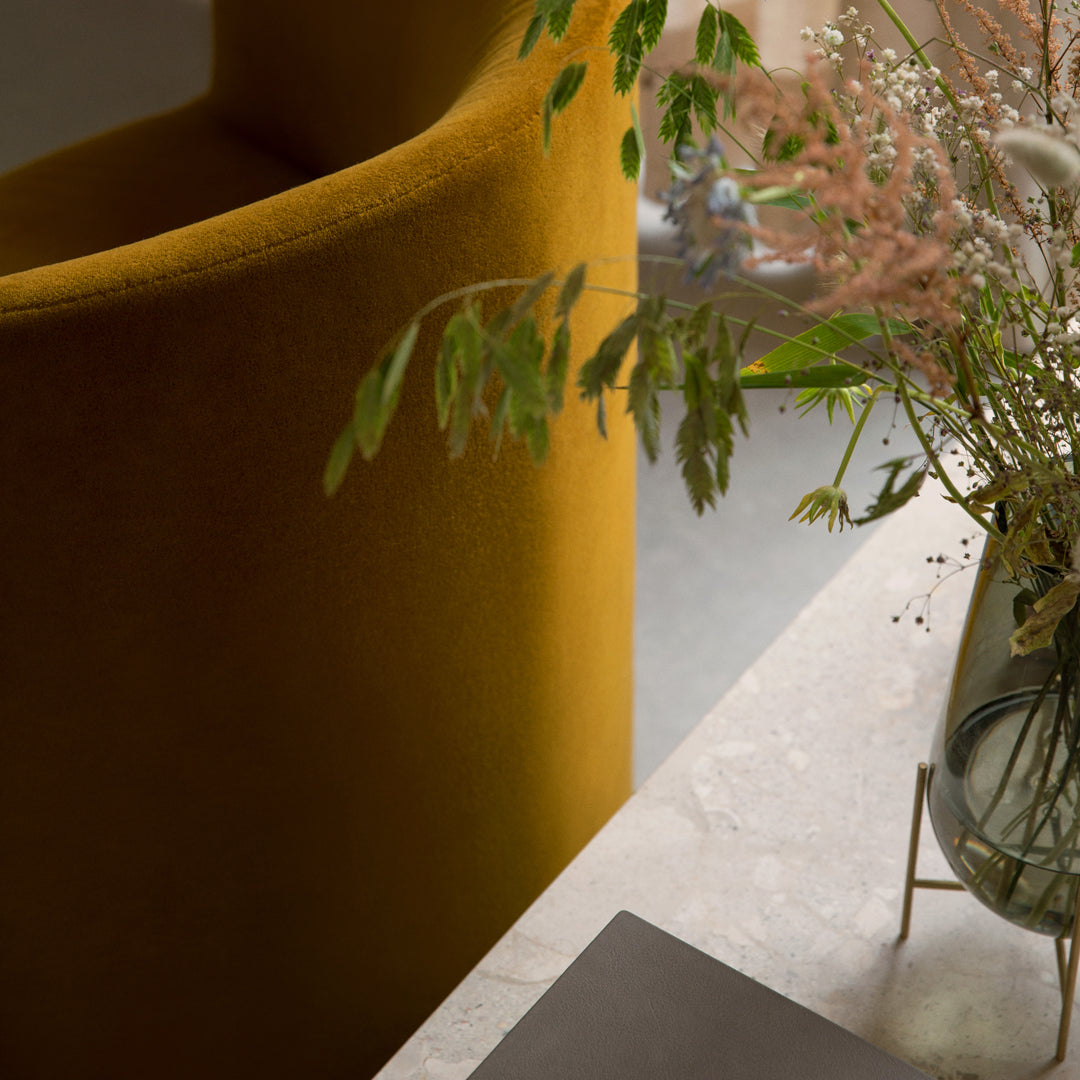 "Yellow velvet chair with soft green leaves and delicate pink blooms on a marble surface."