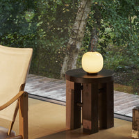 Glowing cream lamp on a dark wooden stool against a backdrop of greenery. Modern, cozy decor accents.