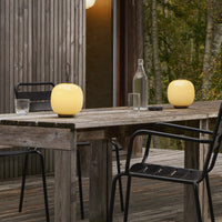 Yellow rounded lamps on a wooden table, contrasted with black metal chairs and a natural backdrop.
