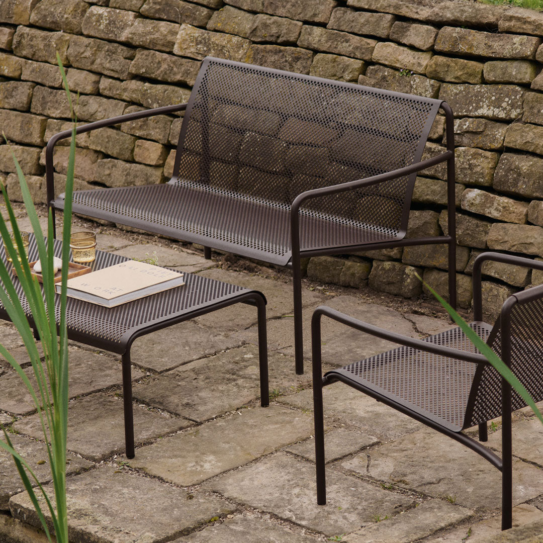 Brown perforated metal patio furniture set against a natural stone wall, featuring subtle green plant accents.