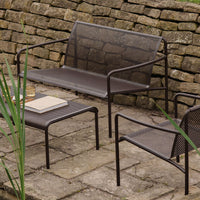 "Modern outdoor furniture set in dark bronze with a perforated pattern, nestled against a rustic stone wall."