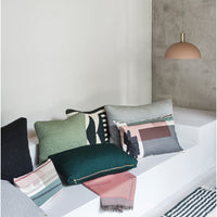 Colorful cushions featuring green, gray, pink, and graphic patterns on a minimalist white couch and concrete backdrop.