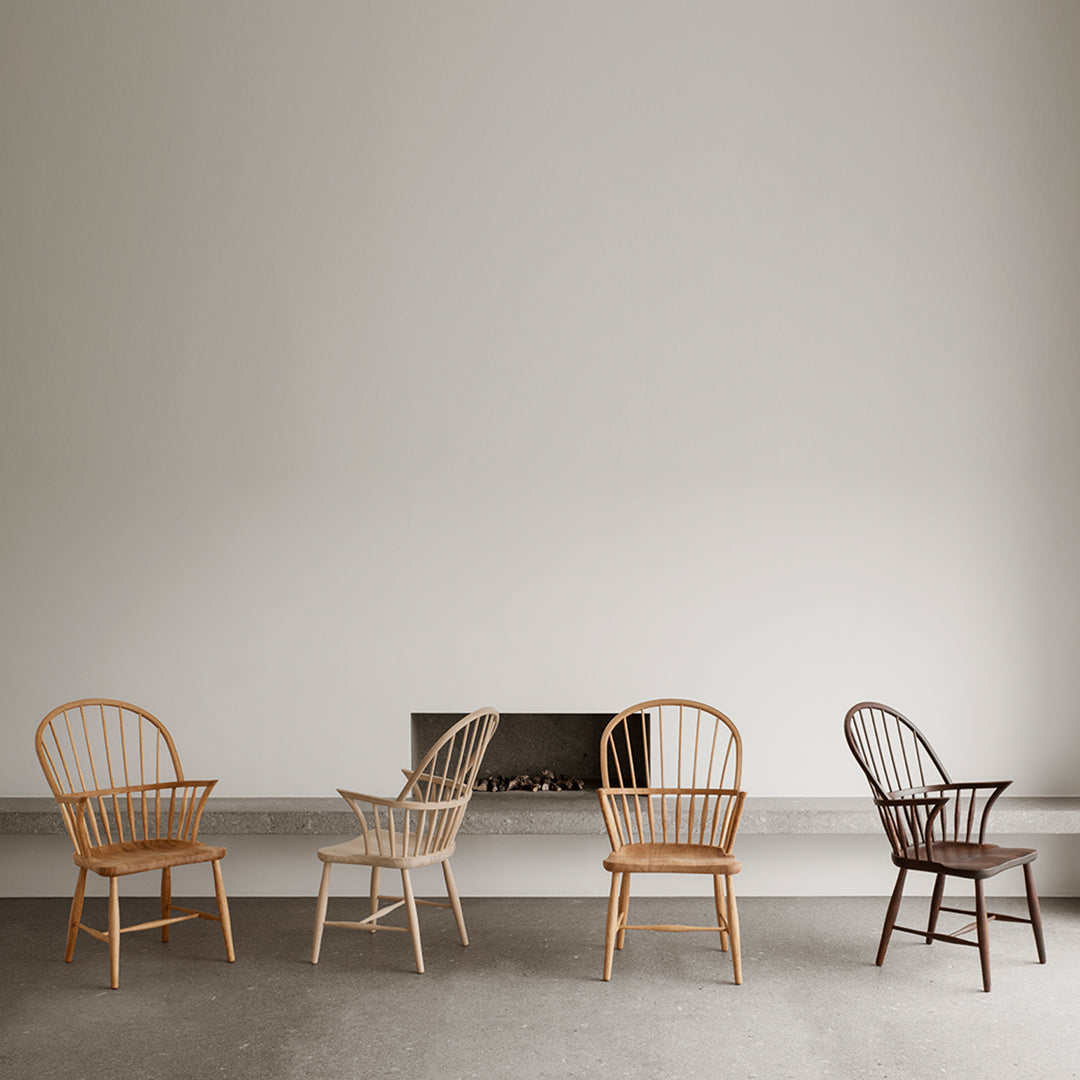 "Four wooden chairs in natural, light beige, and dark brown finishes against a neutral wall."