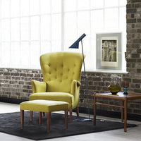 Vibrant yellow tufted armchair and matching ottoman on a black rug, set against a brick wall backdrop.