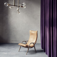 Tan leather chair with sleek curves against a backdrop of deep purple curtains and a subtle gray floor.