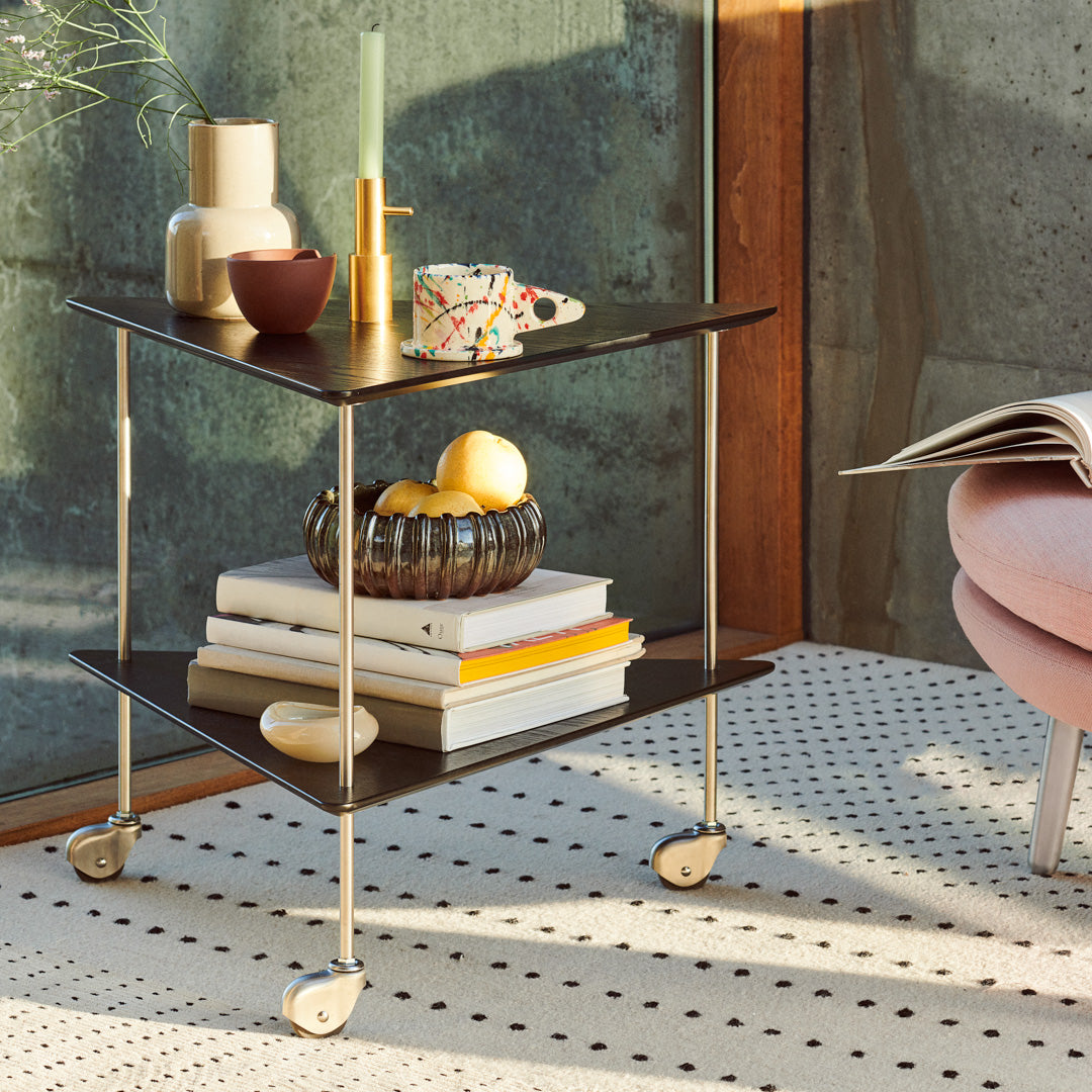 Black and white patterned rolling cart with wooden shelves, accented by colorful decor and a cozy beige rug.
