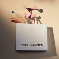 White shopping bag with black text, featuring a pink wall hook and soft beige background with neutral-toned decor.