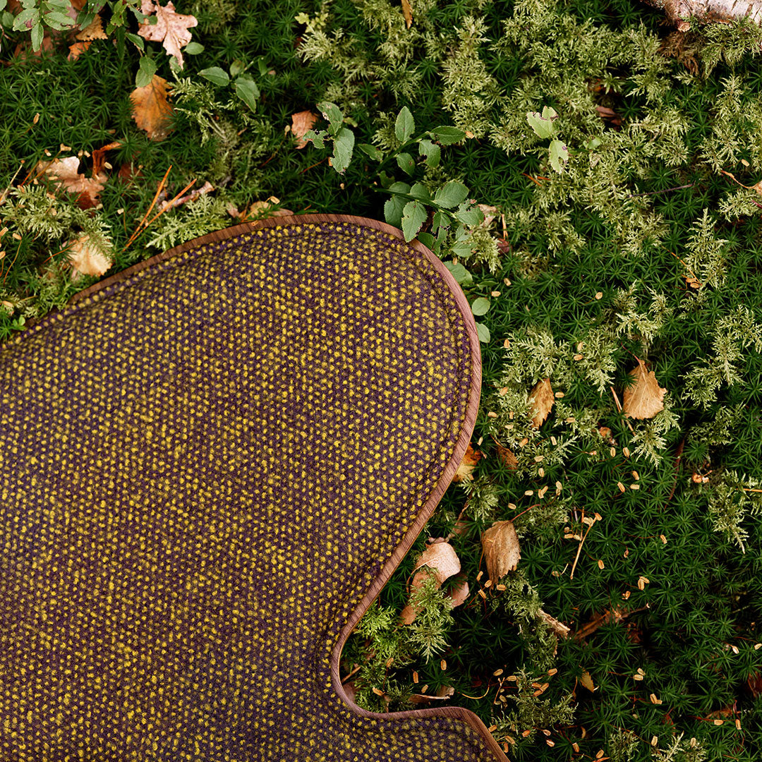 Textured brown and gold pattern on a soft surface, surrounded by green foliage and earthy tones.