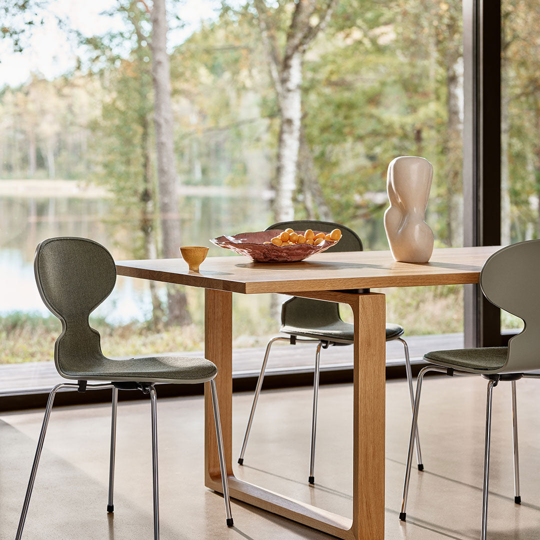Modern dining table with natural wood finish, complemented by green chairs and a ceramic vase for a fresh, stylish look.