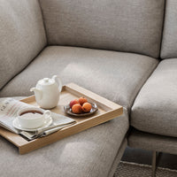Light gray textured upholstery with a soft, neutral palette; accent tray featuring white teapot and vibrant orange fruits.