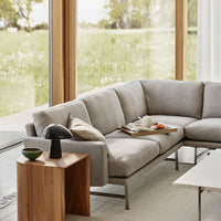 Light gray sectional sofa with clean lines, paired with a wooden side table and soft textures in a bright, airy setting.