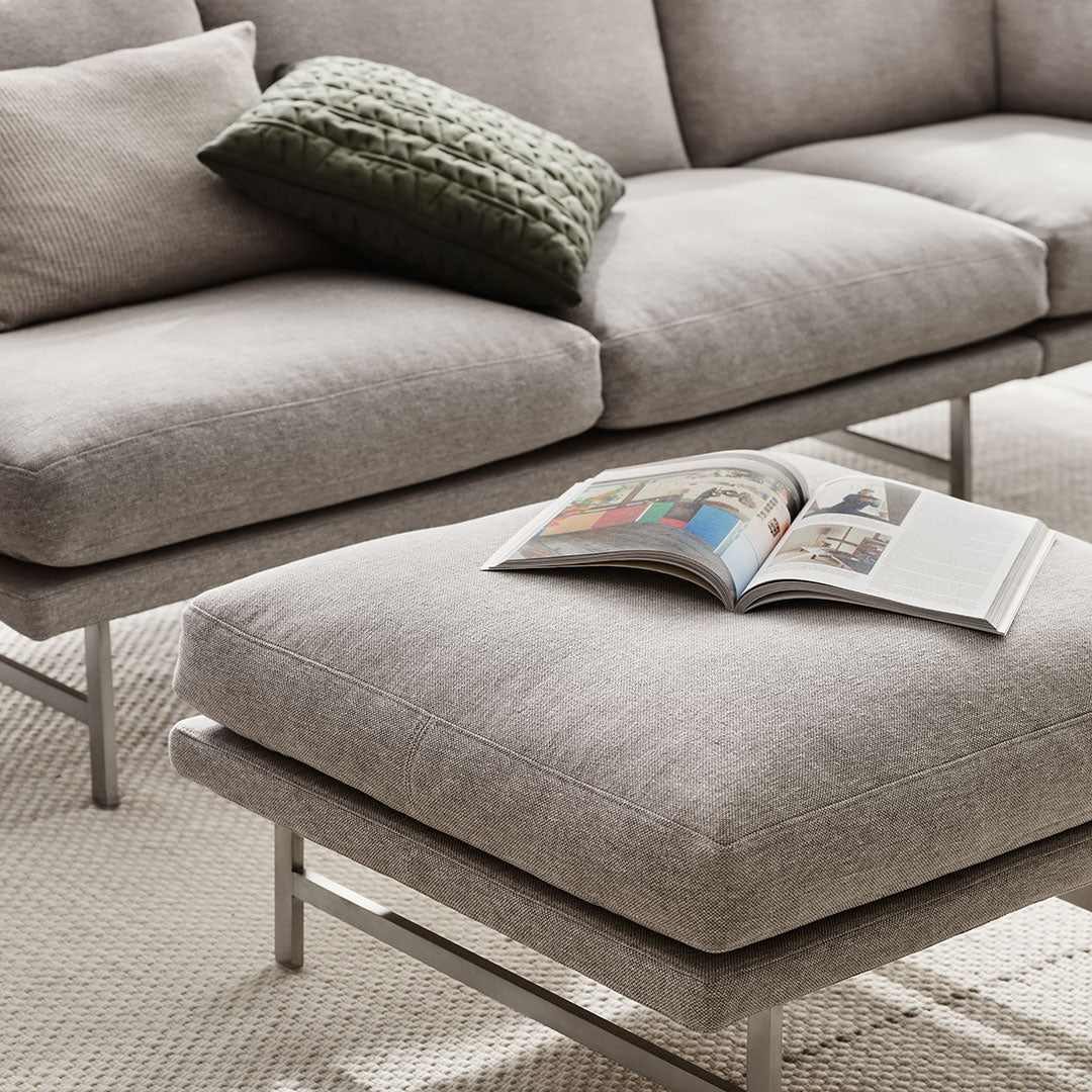 Light gray sofa with textured fabric, complemented by a dark green knitted pillow and a soft, neutral ottoman.