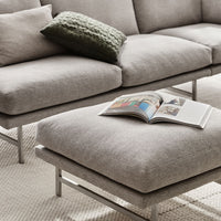 Gray sectional sofa with a green knit cushion and a simple textured ottoman, featuring a light neutral backdrop.