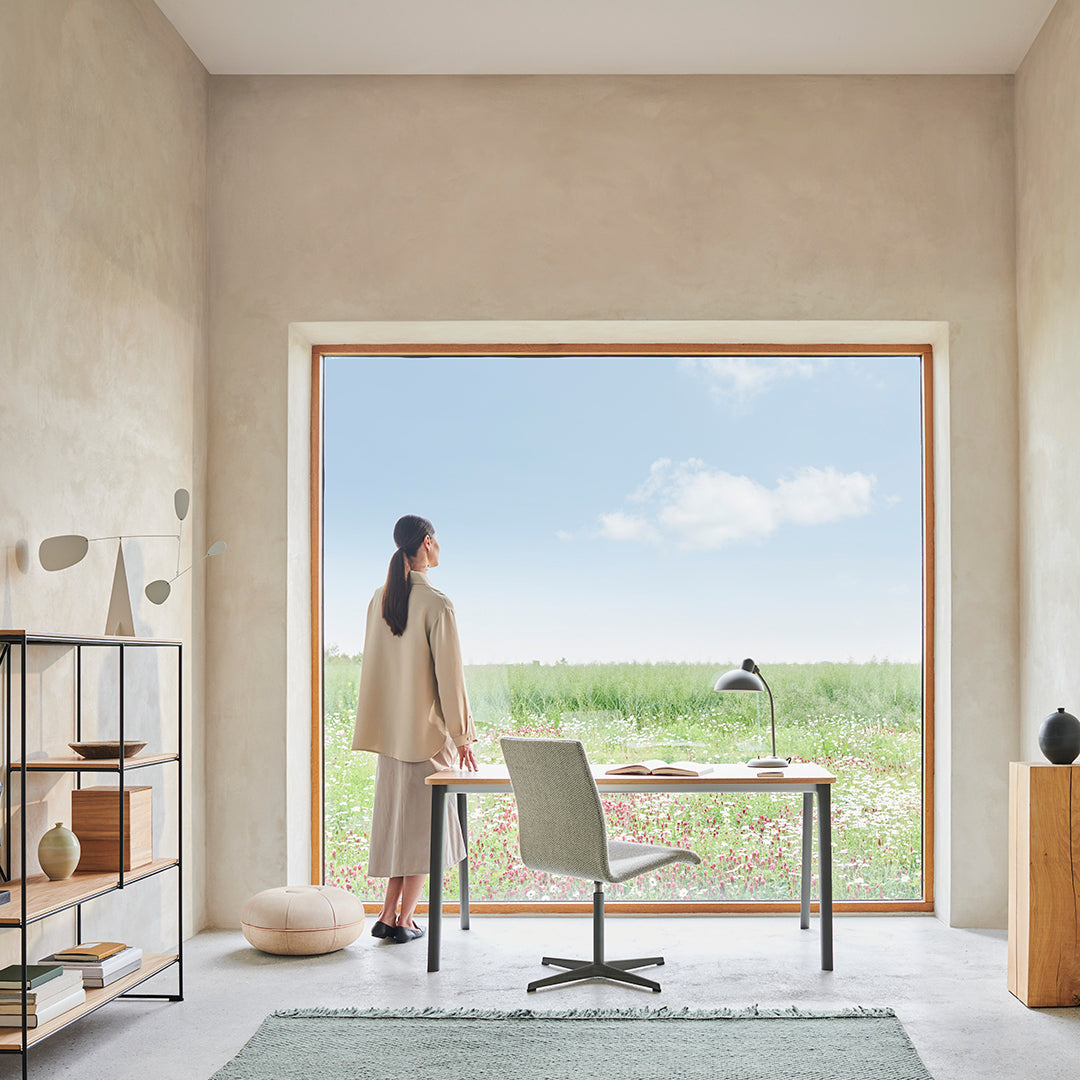 Modern room with soft beige walls, wooden window frame, green rug, and neutral-toned furniture against a floral backdrop.