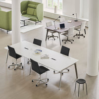 Modern office setup featuring a sleek white table with black chairs and a green lounge chair, all on a light wood floor.
