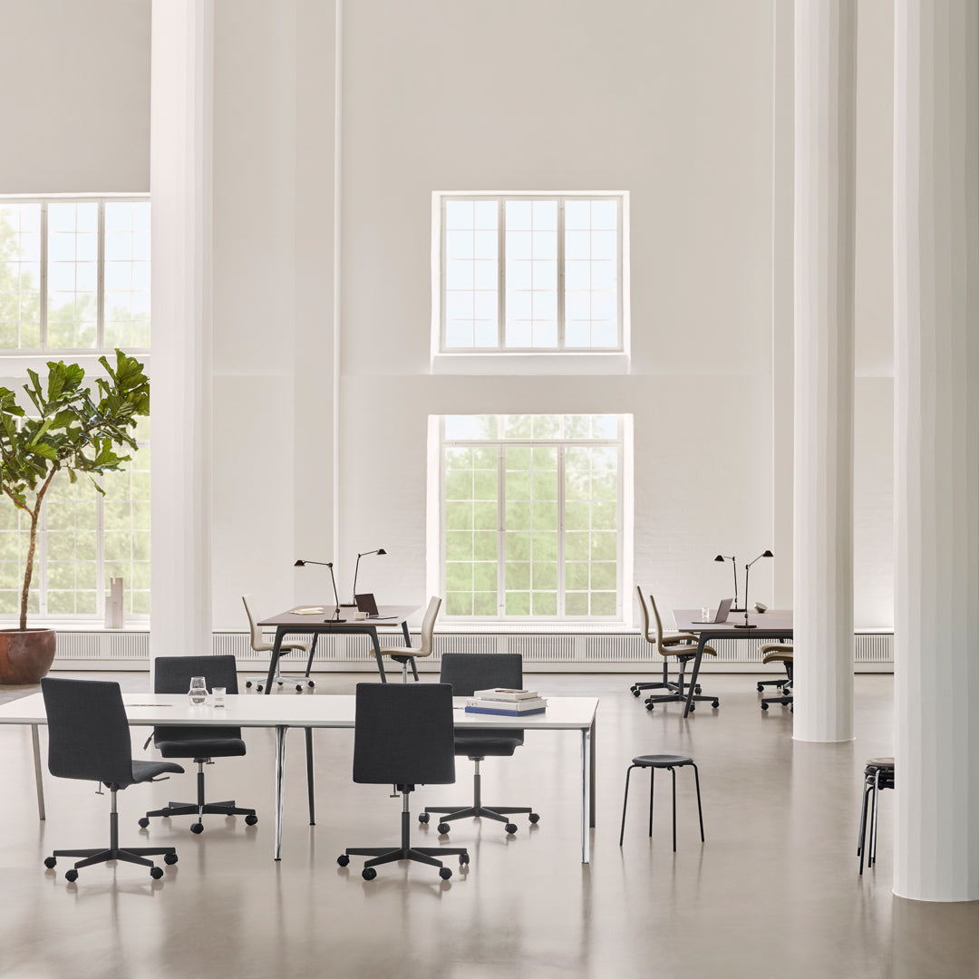 Modern workspace featuring white walls, large windows, and black chairs against a light gray floor.