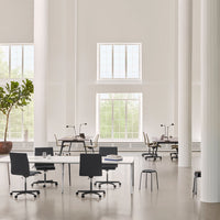 Modern workspace featuring white walls, large windows, and black chairs against a light gray floor.