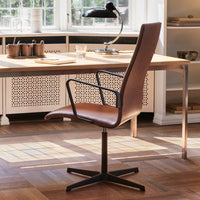 Brown leather office chair with sleek black metal frame, set against a modern interior with warm wooden flooring.