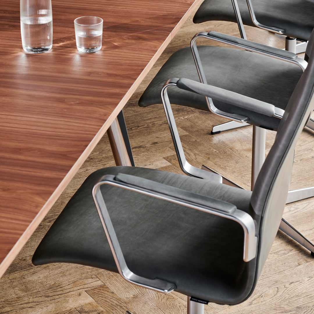 Modern black chairs with chrome accents surrounding a polished wooden table, set on a light wooden floor.