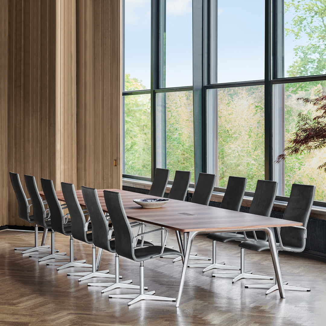 "Modern wooden conference table with sleek black chairs and large windows featuring natural light and greenery."
