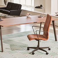 "Brown leather office chair on a geometric pastel patterned rug with a wooden desk in a modern workspace."