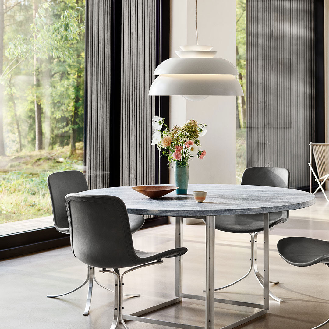 Modern round table with a gray marble top, sleek gray chairs, white pendant light, and a vibrant floral arrangement.