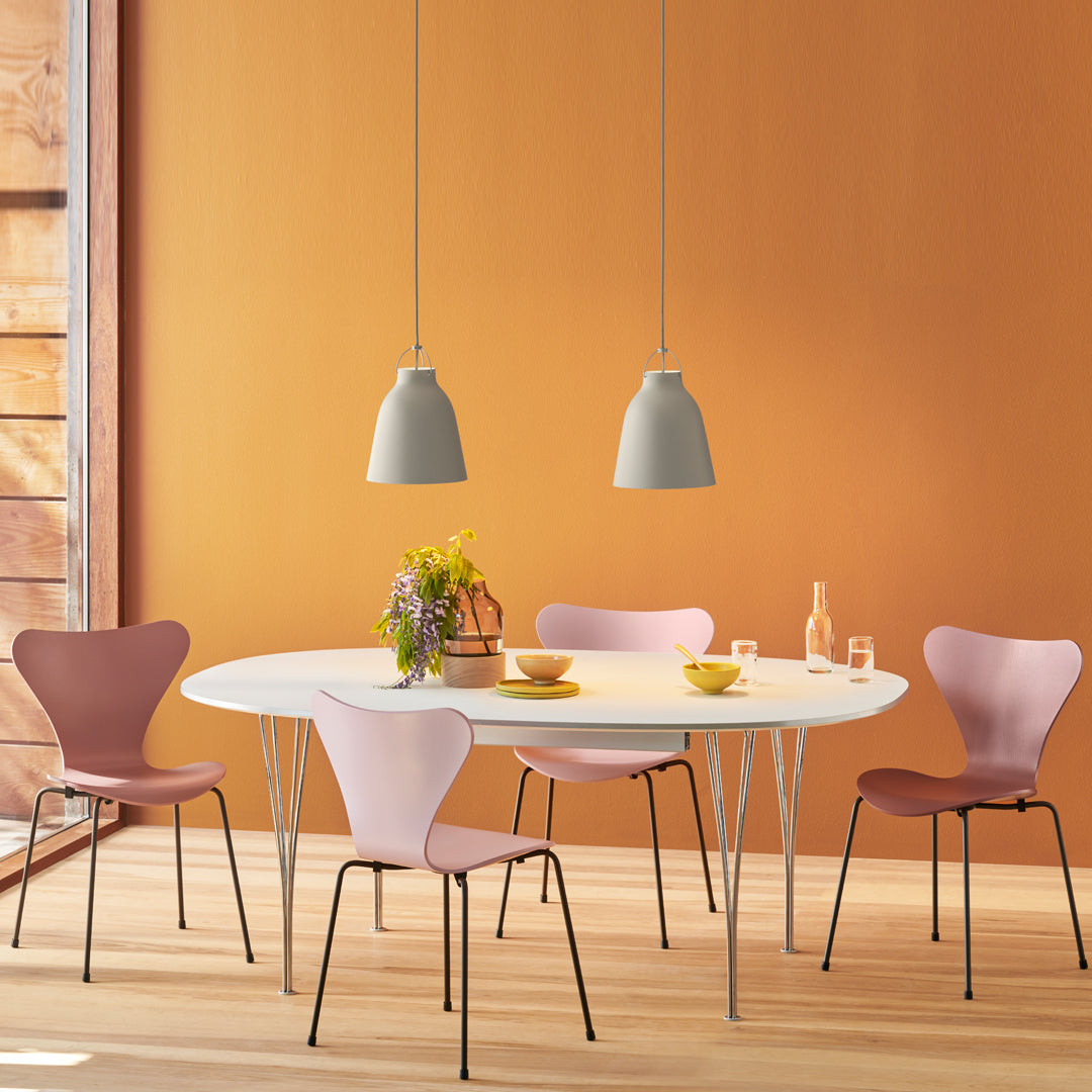 Elegant round table with soft pink and lavender chairs against a warm orange wall, featuring minimalist gray pendant lights.