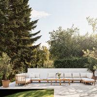 Neutral beige cushions on a wooden sofa set, surrounded by green foliage and natural light, offers a tranquil outdoor vibe.