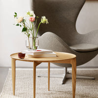Round wooden coffee table with natural finish, placed on a textured light wool rug, enhancing subtle color contrast.