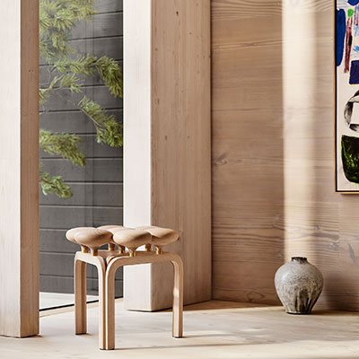 Minimalist wooden stool with a natural finish, featuring smooth curves and warm tones, against a neutral backdrop.