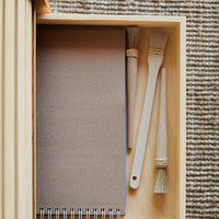 Natural wood drawer with a brown notepad and two brushes, showcasing earthy tones and a minimalistic design.