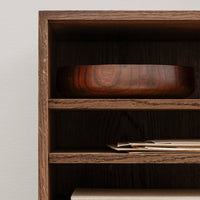 Dark wood bowl on a wooden shelf, showcasing rich brown tones and smooth, glossy finishes.