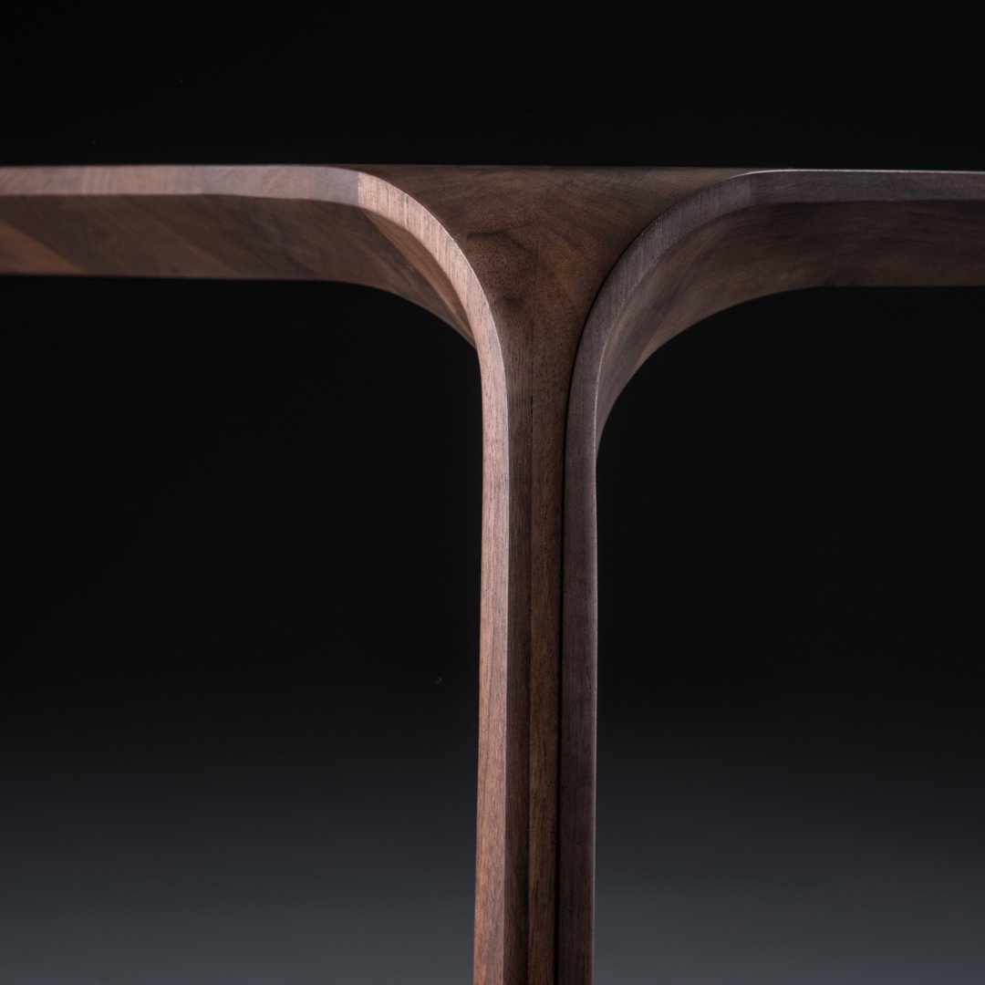 Dark walnut wood table with smooth, curved edges and a modern geometric design against a black background.