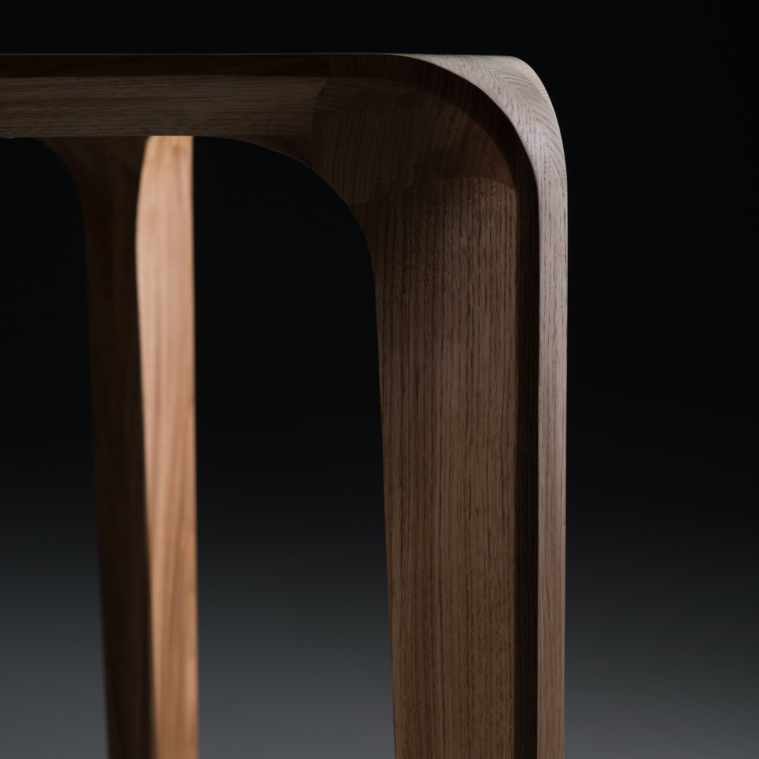 Close-up of a wooden table leg featuring smooth curves and a natural walnut finish against a dark background.