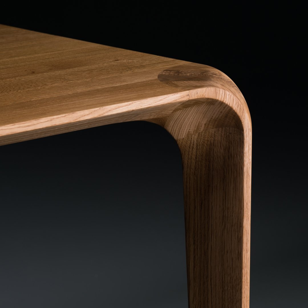 Natural oak wood table with smooth, rounded edges and warm, rich tones against a dark background.