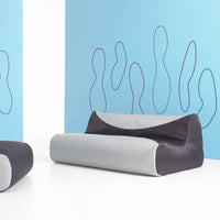 Modern two-tone sofa in gray and black against a pastel blue wall with abstract purple line patterns.