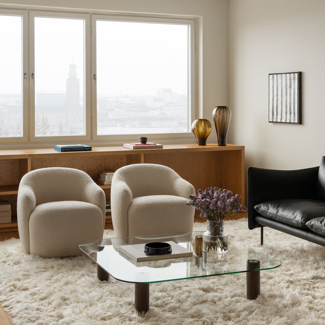 Beige and black chairs with a glass table, set against a neutral-toned room and furry white rug.