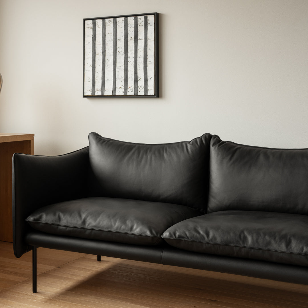 Sleek black leather sofa with smooth cushions and minimalist lines, complemented by a modern striped wall art.