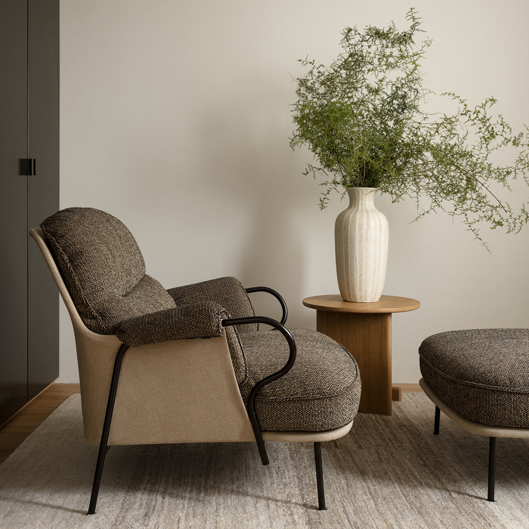 Cozy taupe armchair with textured upholstery, paired with a round, tan ottoman and neutral vase on a light rug.
