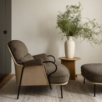Cozy taupe armchair with textured upholstery, paired with a round, tan ottoman and neutral vase on a light rug.