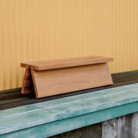 Natural wooden bench with a smooth finish, set against a vibrant yellow corrugated background and rustic blue-green surface.