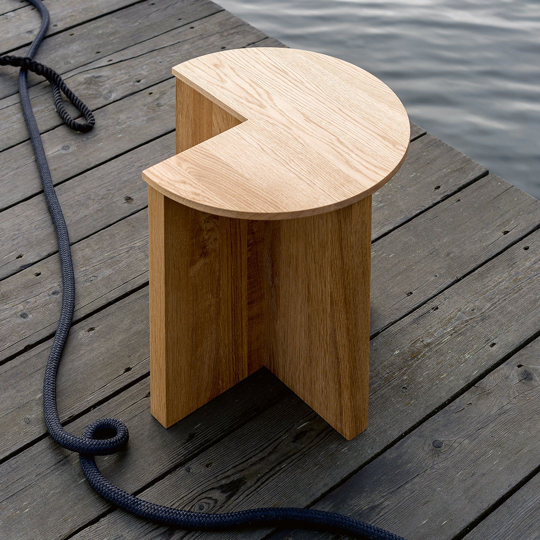 Natural oak wood stool with a minimalist semi-circular design and smooth finish, placed on a wooden dock.